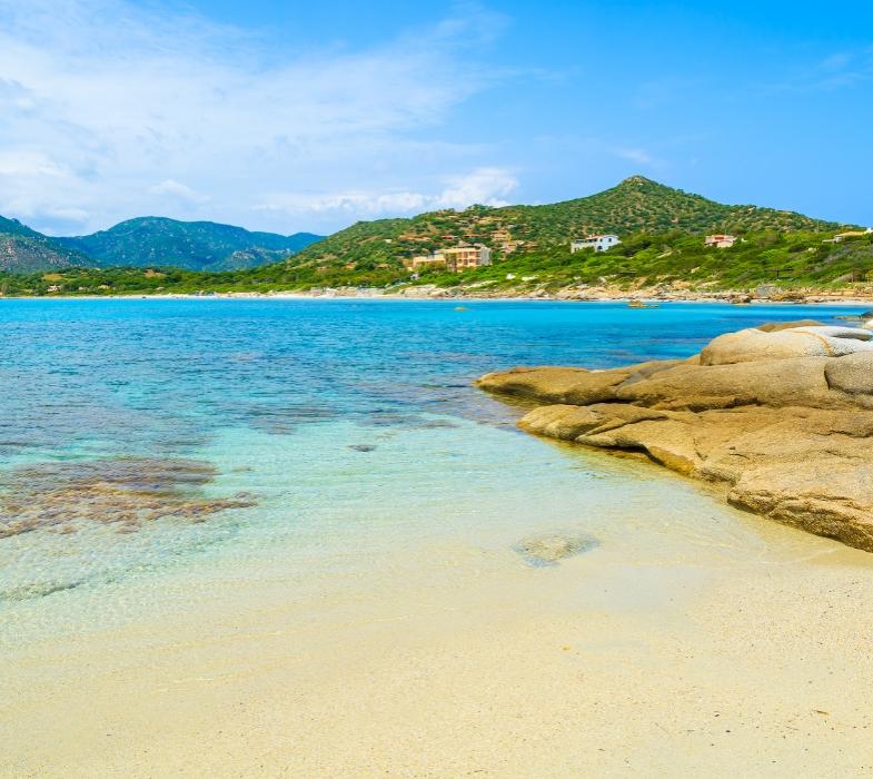 Sentiero sabbioso tra la vegetazione che conduce a una spiaggia con mare azzurro.