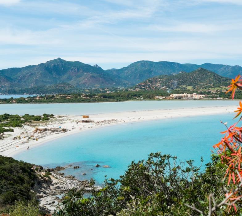 Spiaggia con sabbia bianca e mare turchese, circondata da montagne verdi.