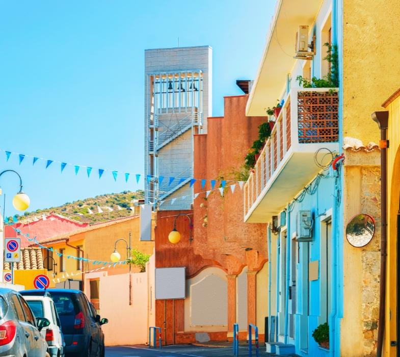 Strada colorata con edifici vivaci e decorazioni di bandierine in un villaggio mediterraneo.
