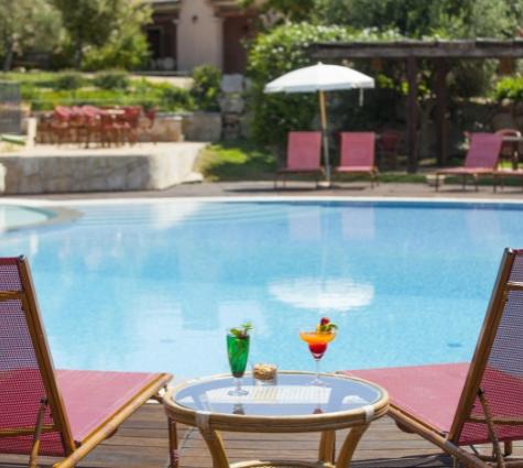 Piscina con sedie a sdraio, tavolino e cocktail colorati in un ambiente rilassante.